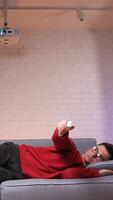vertical man is lying on the comfortable couch and watching TV, he's bored video