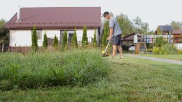 Gardener mows weeds grass. Man cutting grass in yard by using string trimmer. video