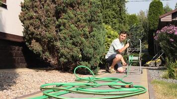 man is winding a watering hose on a reel in the yard of a house video