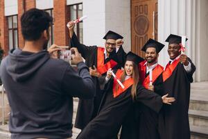 Group of Happy Graduates Celebrating Outside University with Diplomas and Taking Photos