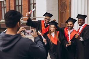 Group of Happy Graduates Celebrating Outside University with Diplomas and Taking Photos