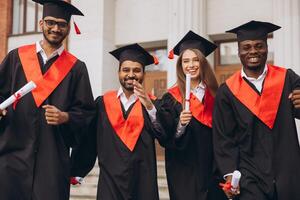 Diverse Group of Happy Graduates Celebrating Together in Cap and Gown Outside University Building photo
