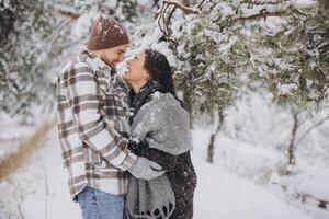 A young happy and loving couple is standing under a pine tree from which snow falls in the mountains in winter. photo