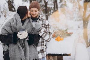 Happy beautiful couple resting and drinking hot tea in the forest in winter in the mountains photo