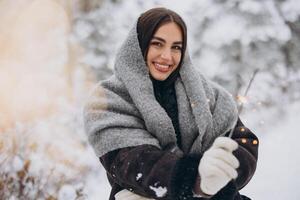 Portrait of happy pretty woman in knitted scarf and mittens holding sparkler and posing in snowy forest photo