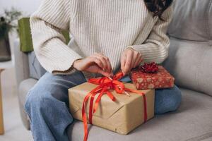 Female hands unwrapping New Year or Christmas presents at home on sofa photo