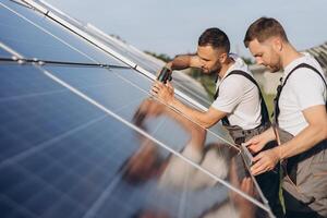 Two skilled workers or craftsmen wearing working gray uniforms, technicians are installing solar panels on a solar farm for clean energy and electricity supply photo