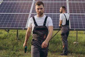 Two skilled workers or craftsmen wearing working gray uniforms, technicians are installing solar panels on a solar farm for clean energy and electricity supply photo