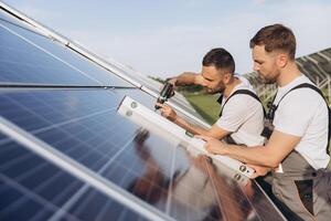 Two skilled workers or craftsmen wearing working gray uniforms, technicians are installing solar panels on a solar farm for clean energy and electricity supply photo