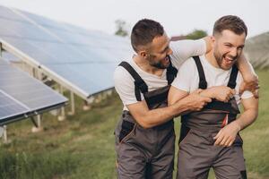Two happy bearded gay in work uniforms joying and flirting with each other hugging on the background of solar panels photo