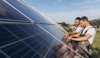 Two skilled workers or craftsmen wearing working gray uniforms, technicians are installing solar panels on a solar farm for clean energy and electricity supply photo