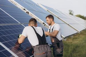 Two skilled workers or craftsmen wearing working gray uniforms, technicians are installing solar panels on a solar farm for clean energy and electricity supply photo