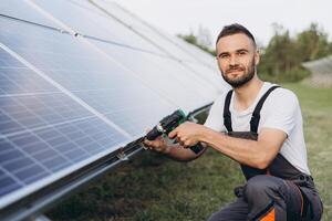 Male bearded technician installing solar panel using electric drill securing solar system installation structure working outdoors - concept of renewable energy construction photo