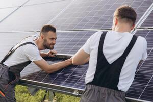 Two skilled workers or craftsmen wearing working gray uniforms, technicians are installing solar panels on a solar farm for clean energy and electricity supply photo