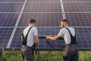 Two skilled workers or craftsmen wearing working gray uniforms, technicians are installing solar panels on a solar farm for clean energy and electricity supply photo