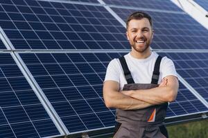 At the forefront of renewable energy innovation, smiling bearded male engineer stands with crossed arms, observing the efficient operation of a newly developed solar panel array photo
