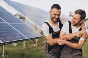 Two happy bearded gay in work uniforms joying and flirting with each other hugging on the background of solar panels photo