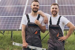 Two happy bearded gay in work uniforms joying and flirting with each other hugging on the background of solar panels photo