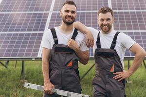 Two happy bearded gay in work uniforms joying and flirting with each other hugging on the background of solar panels photo