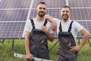 Two happy bearded gay in work uniforms joying and flirting with each other hugging on the background of solar panels photo