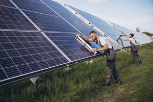 Two skilled workers or craftsmen wearing working gray uniforms, technicians are installing solar panels on a solar farm for clean energy and electricity supply photo