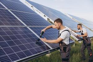 Two skilled workers or craftsmen wearing working gray uniforms, technicians are installing solar panels on a solar farm for clean energy and electricity supply photo