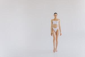 Full-length portrait of beautiful woman with slim body in underwear posing in the white studio background with copy space, mock-up photo