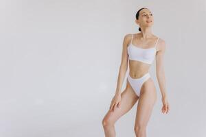Portrait of beautiful woman with slim body in underwear posing in the white studio background with copy space, mock-up photo