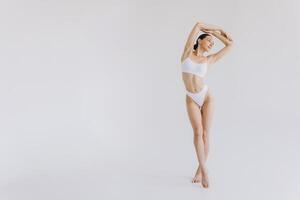 Full-length portrait of beautiful woman with slim body in underwear posing in the white studio background with copy space, mock-up photo