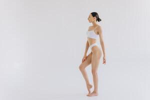 Full-length portrait of beautiful woman with slim body in underwear posing in the white studio background with copy space, mock-up photo