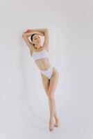 Full-length portrait of beautiful woman with slim body in underwear posing in the white studio background with copy space, mock-up photo