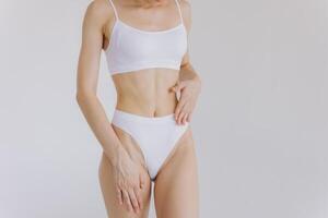 Close up shot of unrecognizable fit woman in lingerie isolated on white background. Torso of slim attractive female with flat belly in white underwear. Copy space for text. photo