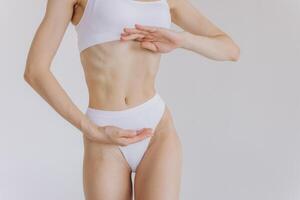 Close up shot of unrecognizable fit woman in lingerie isolated on white background. Torso of slim attractive female with flat belly in white underwear. Copy space for text. photo