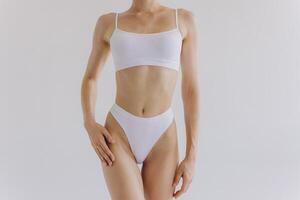 Close up shot of unrecognizable fit woman in lingerie isolated on white background. Torso of slim attractive female with flat belly in white underwear. Copy space for text. photo
