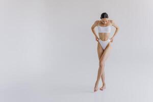 Full-length portrait of beautiful woman with slim body in underwear posing in the white studio background with copy space, mock-up photo