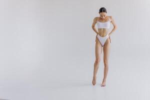 Full-length portrait of beautiful woman with slim body in underwear posing in the white studio background with copy space, mock-up photo