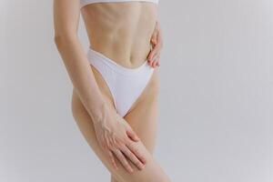 Close up view. Crop image of woman with slim body and perfect stomach in underwear posing in the white studio background. photo