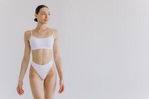 Portrait of beautiful woman with slim body in underwear posing in the white studio background with copy space, mock-up photo