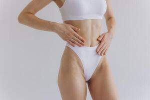 Close up view. Crop image of woman with slim body and perfect stomach in underwear posing in the white studio background. photo