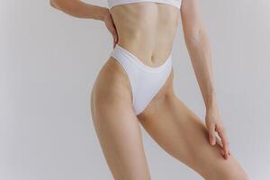 Close up view. Crop image of woman with slim body and perfect stomach in underwear posing in the white studio background. photo