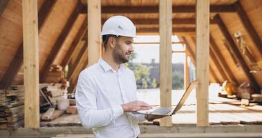 Man builder. Foreman with laptop. Contractor for construction company. Architect in unfinished building. Builder in wooden house under construction. Man engineer from construction team photo