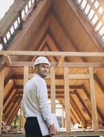 Man builder. Rear view of foreman with laptop. Contractor for construction company. Architect in unfinished building. Builder in wooden house under construction. Man engineer from construction team photo