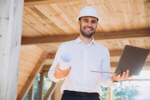 Man builder. Foreman with laptop. Contractor for construction company. Architect in unfinished building. Builder in wooden modular house under construction. Man engineer from construction team photo