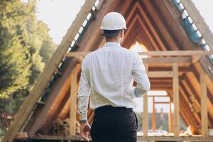 Rear view of construction engineer in white helmet. Developer with construction documentation on the background of wooden modular building under construction. photo