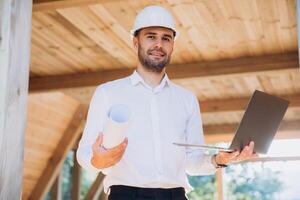Man builder. Foreman with laptop. Contractor for construction company. Architect in unfinished building. Builder in wooden modular house under construction. Man engineer from construction team photo
