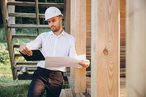 Foreman studies blueprints with tablet. Contractor for construction company. Architect in unfinished building. Builder in wooden house under construction. Man engineer from construction team photo