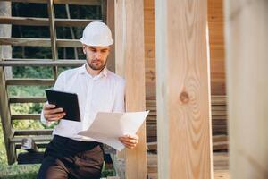 Foreman studies blueprints with tablet. Contractor for construction company. Architect in unfinished building. Builder in wooden house under construction. Man engineer from construction team photo