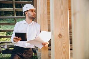 Foreman studies blueprints with tablet. Contractor for construction company. Architect in unfinished building. Builder in wooden house under construction. Man engineer from construction team photo
