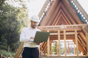 Man builder. Foreman with laptop. Contractor for construction company. Architect in unfinished building. Builder in wooden house under construction. Man engineer from construction team photo