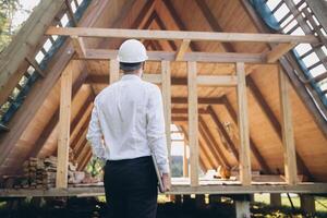 Man builder. Rear view of foreman with laptop. Contractor for construction company. Architect in unfinished building. Builder in wooden house under construction. Man engineer from construction team photo